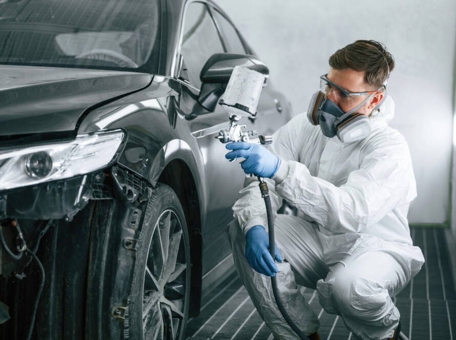 Profesjonalny pracownik malujący samochód przy użyciu pistoletu natryskowego